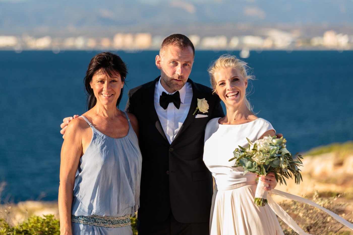 Ein hübsches Gruppenbild mit dem Brautpaar und dem Meer im Hintergrund.